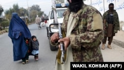 A woman wearing a burqa with a child walk past Taliban fighters along a roadside in Jalalabad, Afghanistan. (file photo)