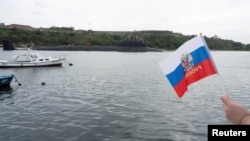 A member of Havana's Russian community held a flag as a Russian nuclear-powered submarine entered the bay of the Cuban capital in the last Russian naval visit, on June 12.