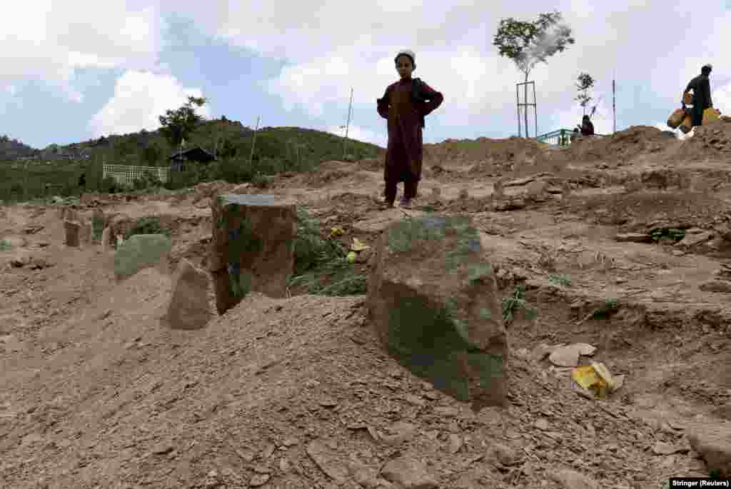 An Afghan boy stands near the graves of his relatives who died in the earthquake in Gayan.