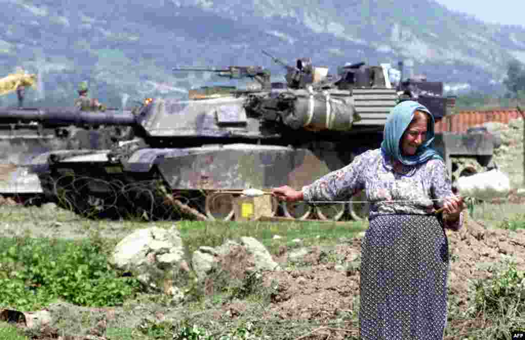 Албанська жінка пряде вовну перед американським танком M1 Abrams, який був частиною операції НАТО під час конфлікту в Косові, біля авіабази Рінас,12 травня 1999 року. З екіпажем із чотирьох осіб (командир, навідник, заряджальник і водій) «Абрамс» є одним із найважчих танків на озброєнні, вагою в майже 62 метричні тонни 